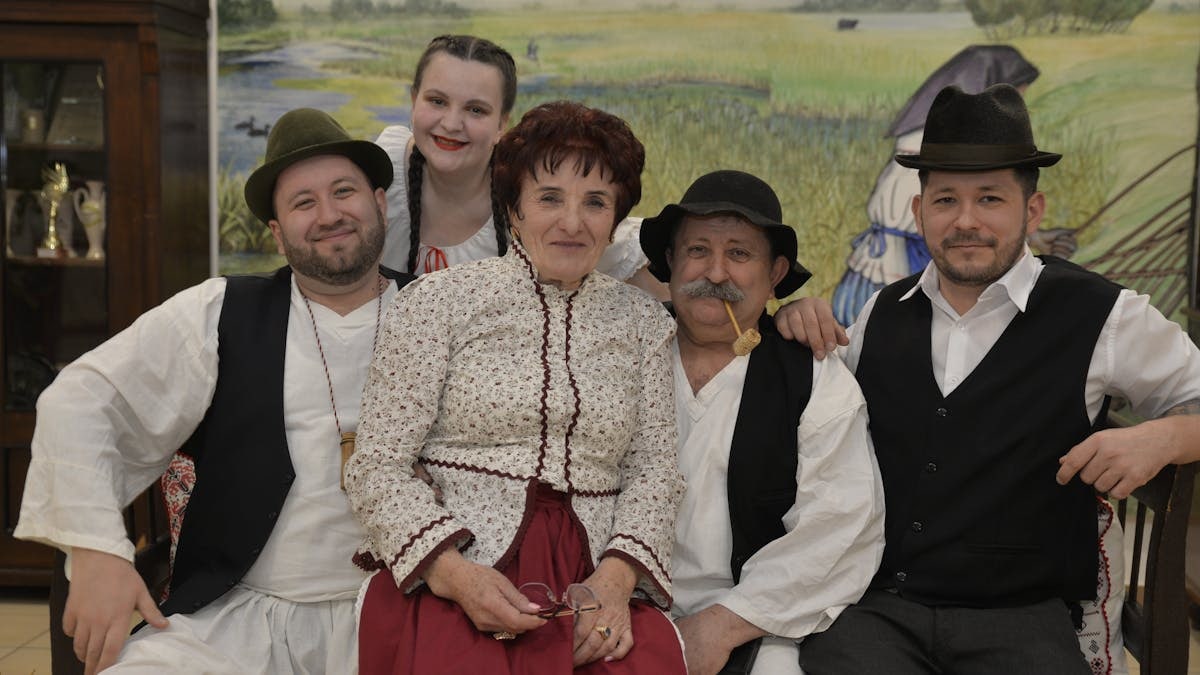 A Hungarian family dressed in traditional folk clothing poses indoors, exuding cultural heritage.